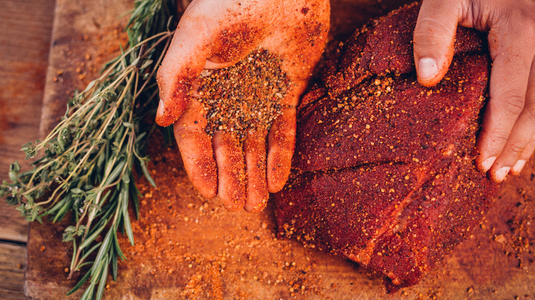 A person applying dry rub to steak