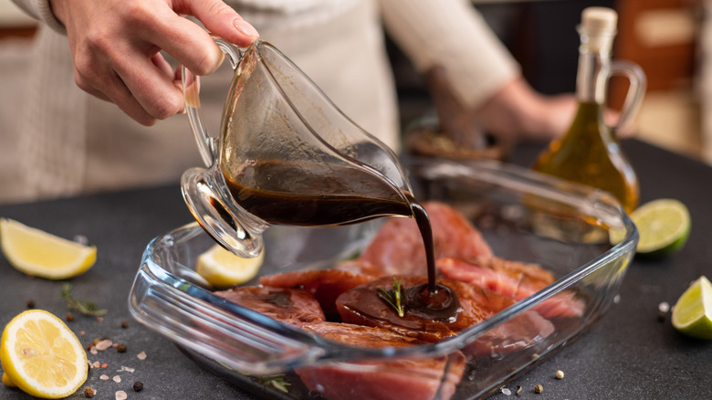 pouring a marinade into a glass dish with raw meat