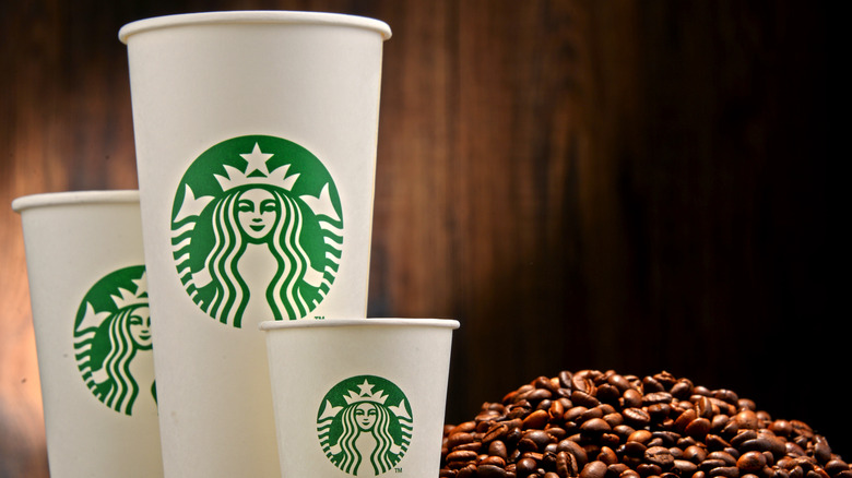 Three Starbucks cups sit next to a pile of coffee beans.