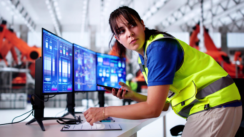 Woman in fluorescent work vest taking info from computer while looking over her shoulder
