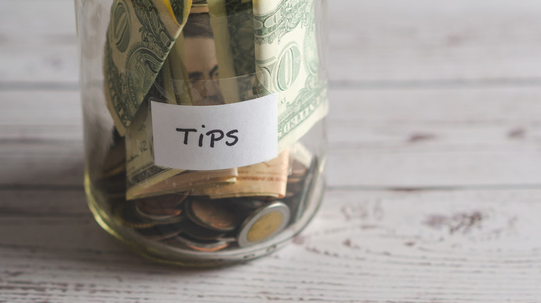Glass tip jar with cash in it on a painted wood table