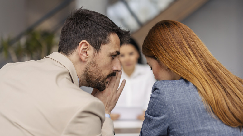Man telling something confidential to a woman in an office setting