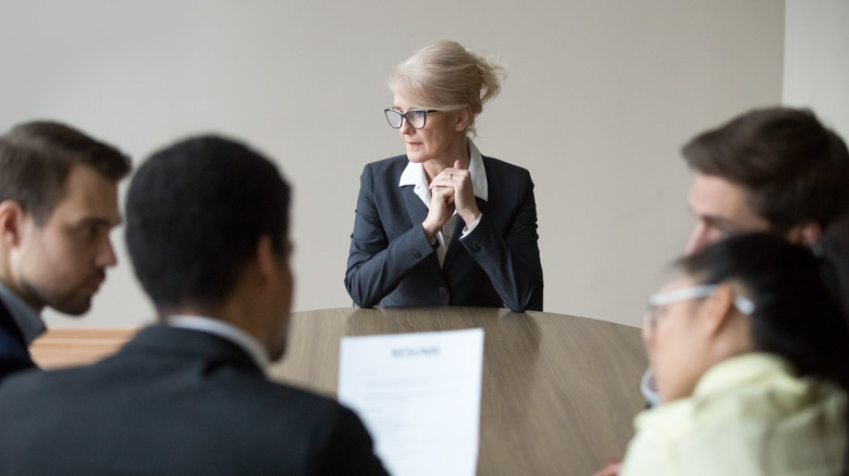 An older woman sits at a table with four younger people evaluating her resume