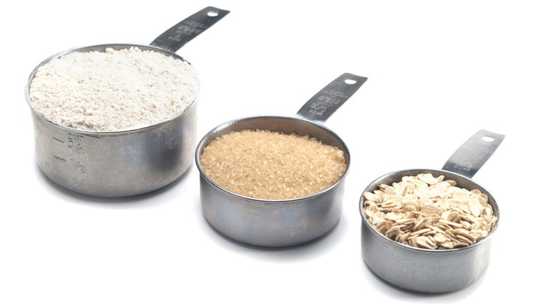Different sized measuring cups filled with flour, sugar, and oats on a white background