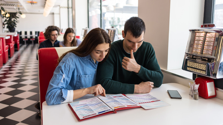 Couple sitting on the same side of a booth and looking at a restaurant menu