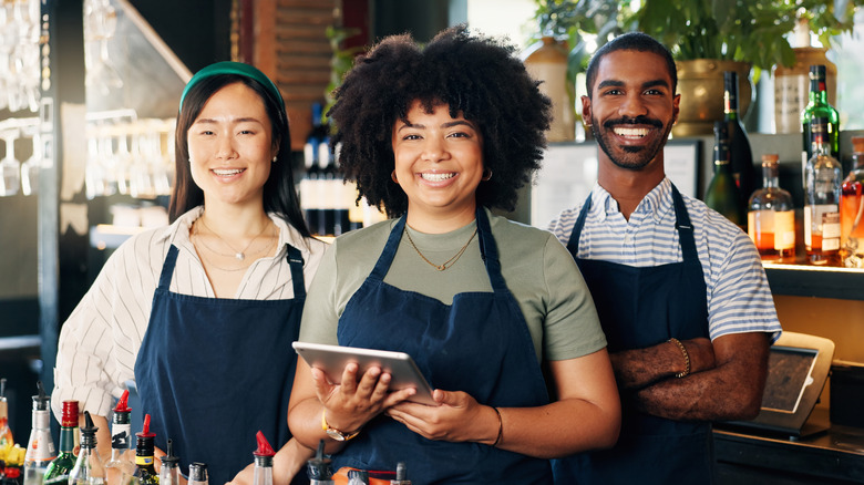Three smiling restaurant servers wearing aprons
