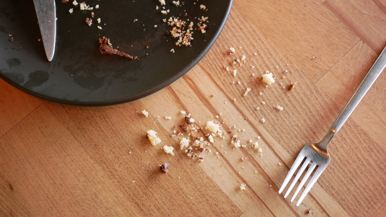 Empty plate with silverware and crumbs on a wooden table