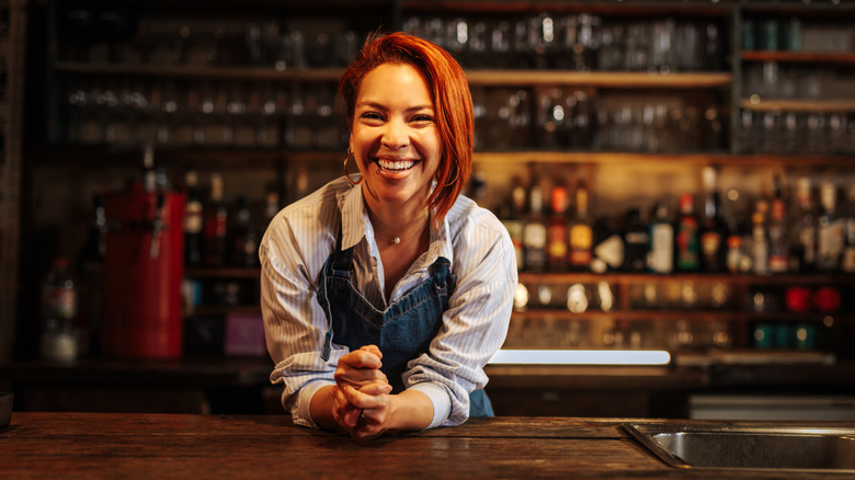 Female bartender leaning over bar with a big smile