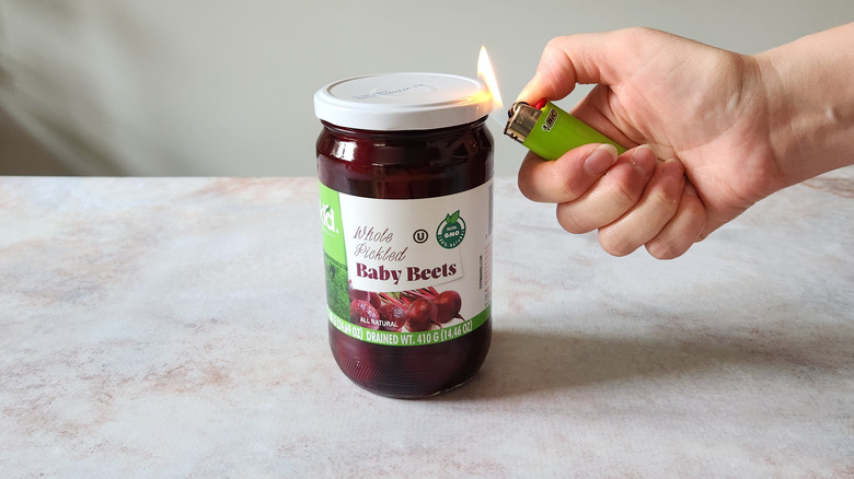 A woman's hand is shown using a lighter to warm up the seal of a jar.