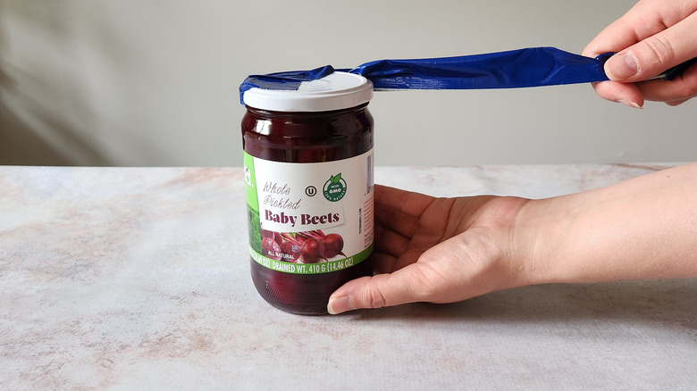 A woman's hands are shown using duct tape to open a jar.