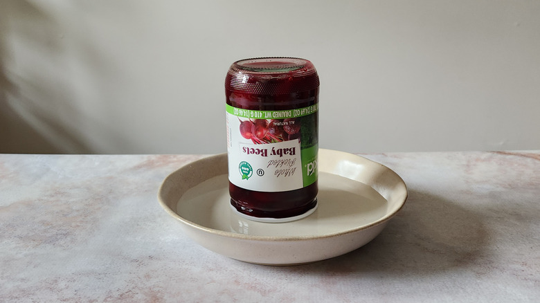 An upside-down jar is resting in a shallow bowl of water on a table.
