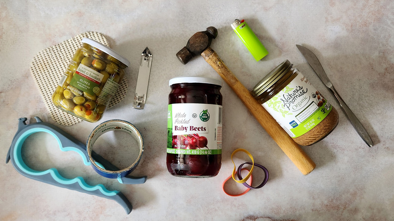 Three jars and assorted jar-opening tools are displayed on a marble table.