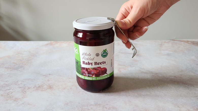 A woman's hand is shown using a bottle opener to open a jar.