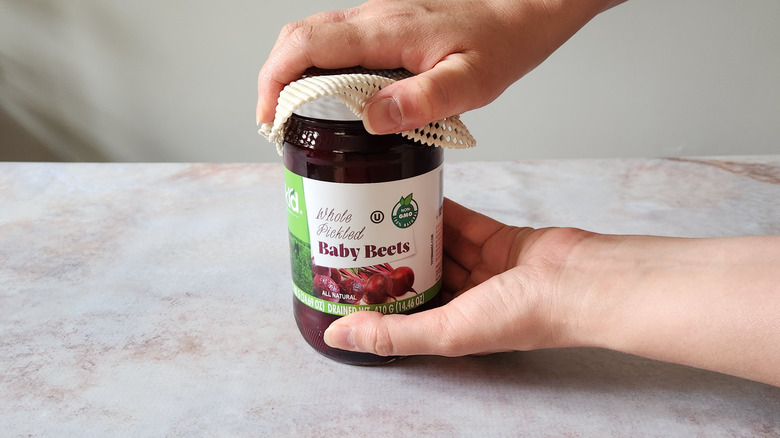 A woman's hands are shown using a rubber gripper tool to open a jar.