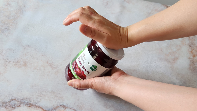 A woman's hands are shown using the water hammer method to break the seal on a jar.
