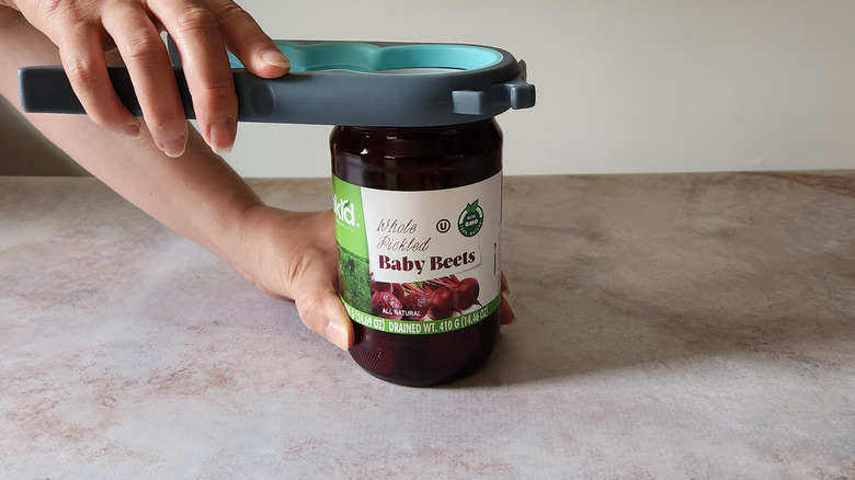 A woman's hands are shown using a jar-opening tool to open a jar.