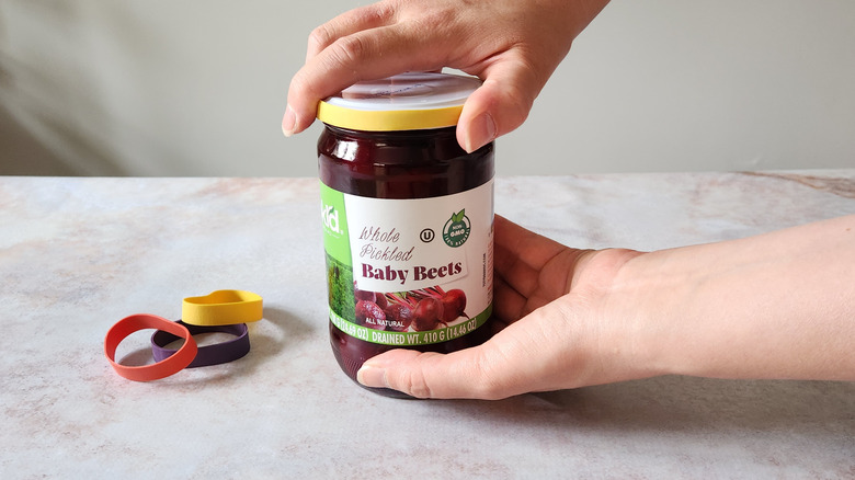 A woman's hands are shown using a rubber band to open a jar.