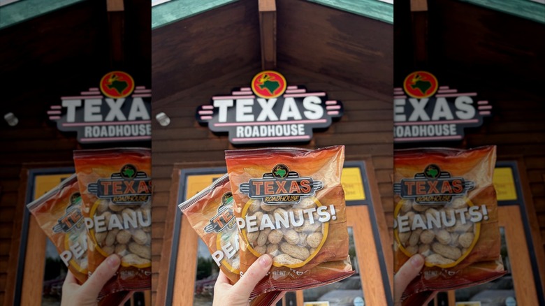Hand holding bags of peanuts in front of the entrance to a Texas Roadhouse location