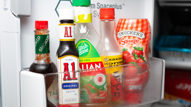 Bottles of Tabasco, A.1., Wish Bone Italian dressing, Kikkoman mirin, and Smucker's jam in a refrigerator door