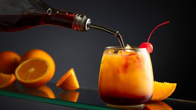 Pouring grenadine into a Tequila Sunrise with oranges in the background