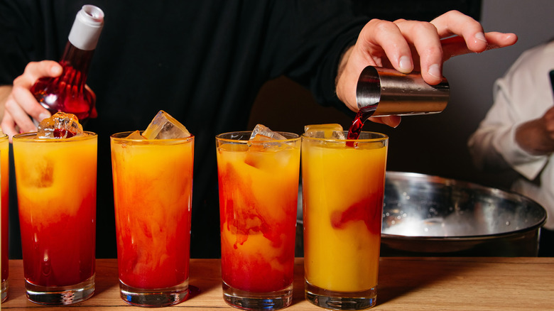 Hands pouring grenadine into Tequila Sunrise cocktails