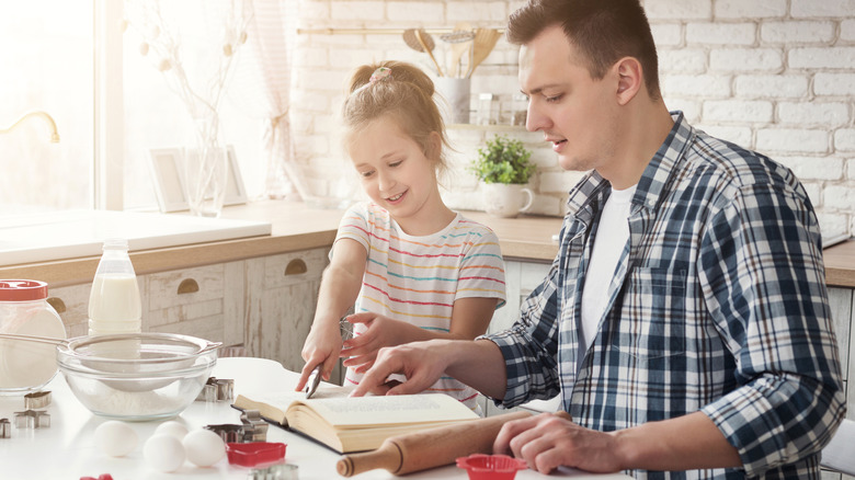 Father and daughter reading recipe in cookbook