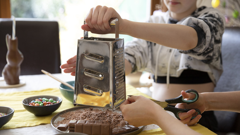 Child holding grater with chocolate on table