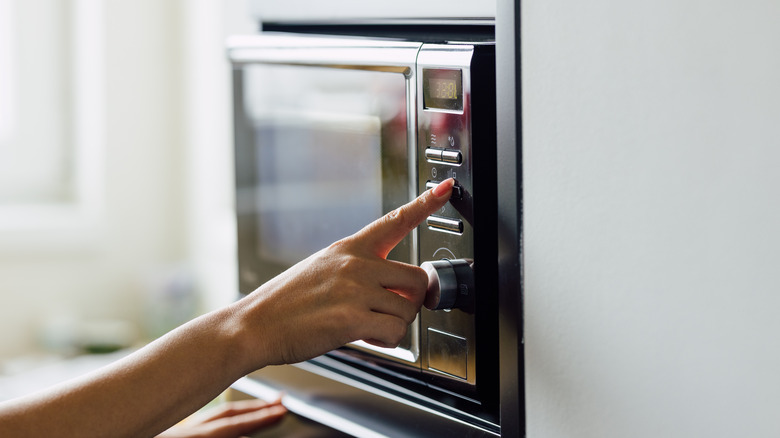 Hand presses buttons on black microwave