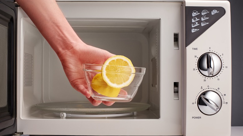 Hand places glass bowl with lemons into microwave