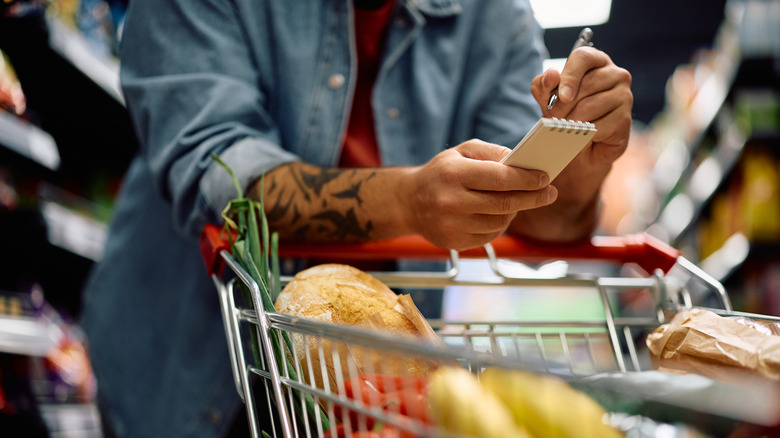 A person holding a grocery list and checking off items