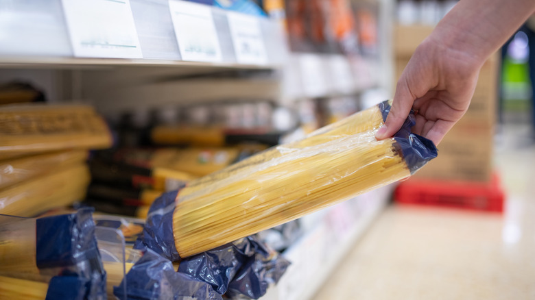 Someone taking pasta off the shelf in a grocery store