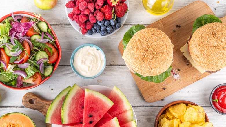 Picnic table topped with summer salads, fruit, and sandwiches