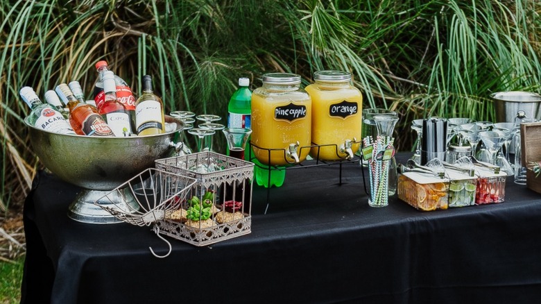 Outdoor bar with tub of liquor, juices, fruit garnishes, and glassware