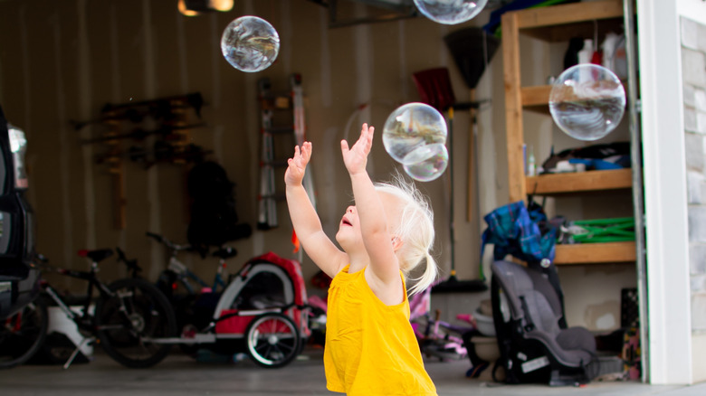 Little girl in yellow shirt popping bubbles in front of an open garage