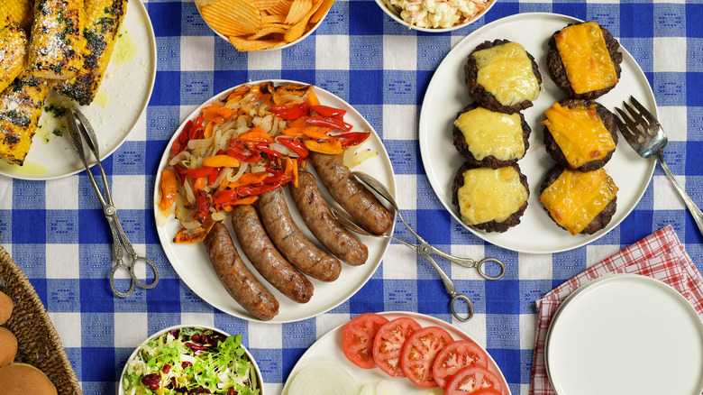 Blue gingham tablecloth with white plates of grilled food, condiments, and sides
