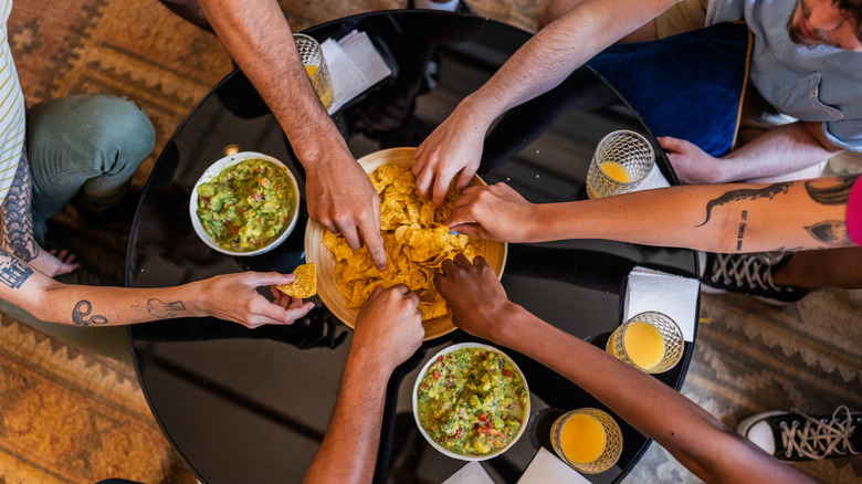 People eat guacamole with chips around a table