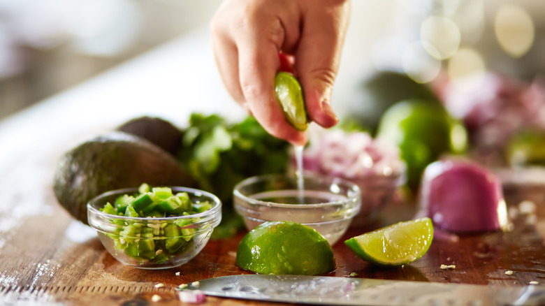A hand squeezes lime juice alongside other ingredients for guacamole