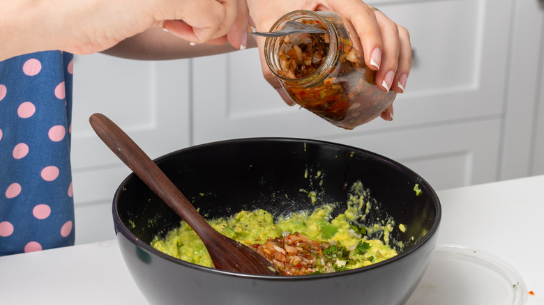 Salsa is poured into a bowl of guacamole