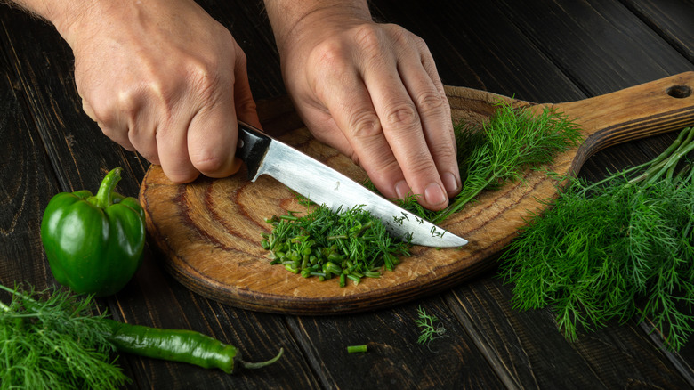 Dill is chopped on a cutting board next to peppers