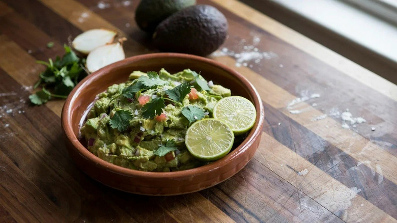 A bowl of guacamole sits on a prep table