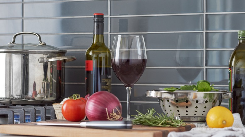 Glass and bottle of red wine with ingredients for a recipe and a stock pot on the stove