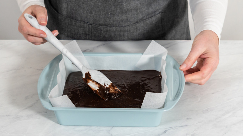 Brownie batter in light blue pan lined with parchment paper on white counter