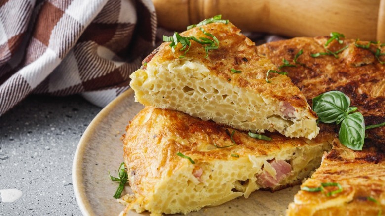 Spaghetti pie slice with herbs on a stone plate