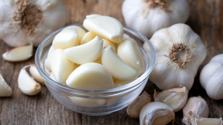 garlic cloves in a small glass bowl with garlic bulbs around