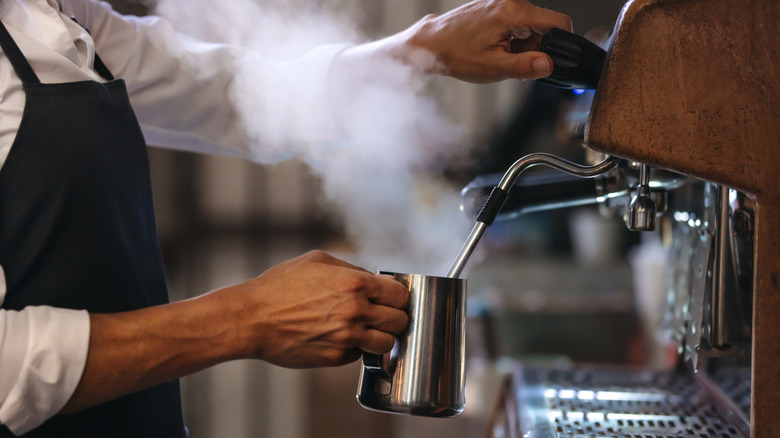 Barrista using a coffee steaming wand and silver pitcher