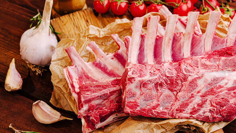 A few racks of lamb on paper surrounded by whole garlic and tomatoes