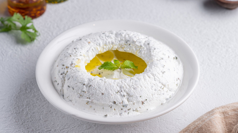 A bowl of yogurt, herbs, and olive oil on a white background