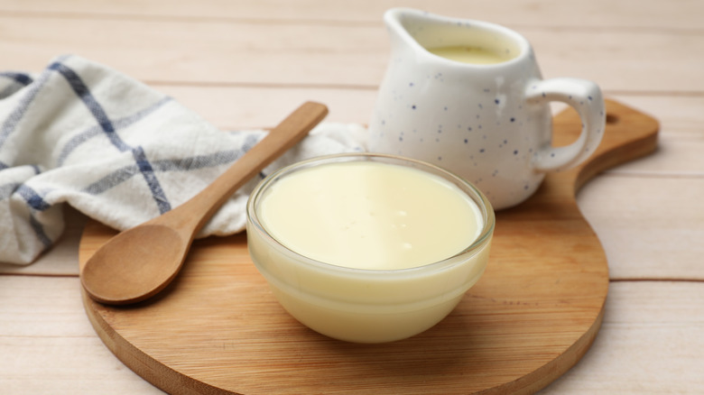 A dish of evaporated milk next to a tiny milk pitcher, a wooden spoon and a striped white towel