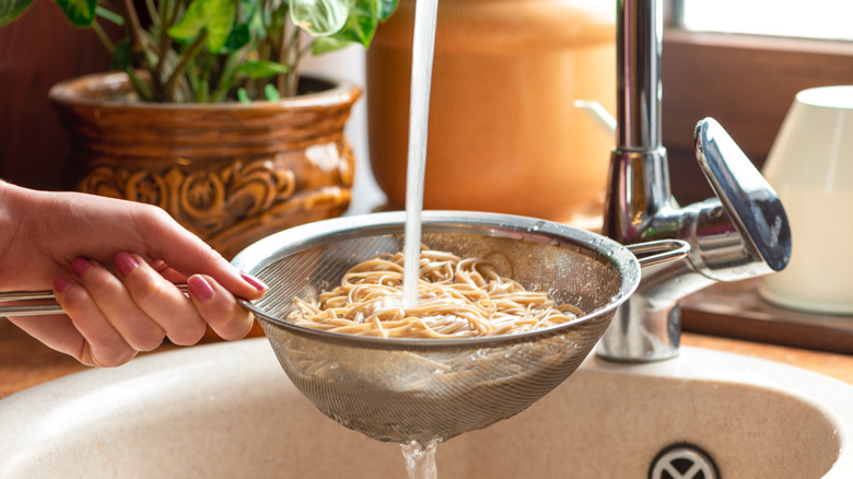 A person rinsing pasta in a colander at a kitchen sink
