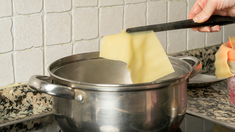 A person removing larged cooked pasta noodle from a pot with tongs